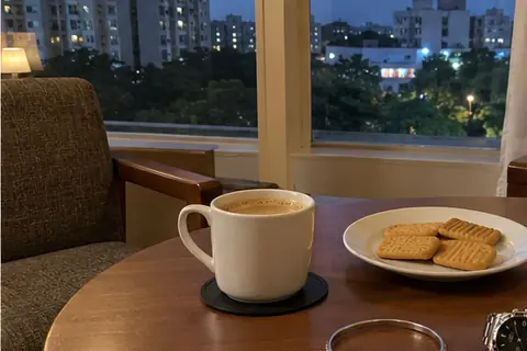 Chai and biscuits on a table by a hotel room window, a silver bangle beside the cup